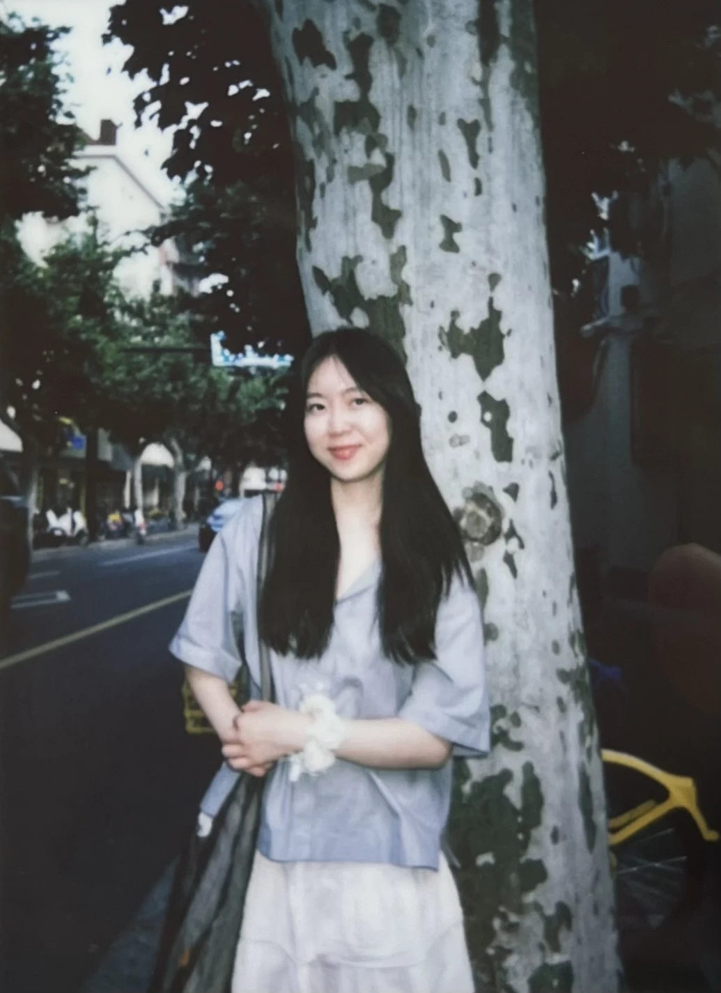 Carolyn, the photographer, leaning against a plane tree on a street, shot on film